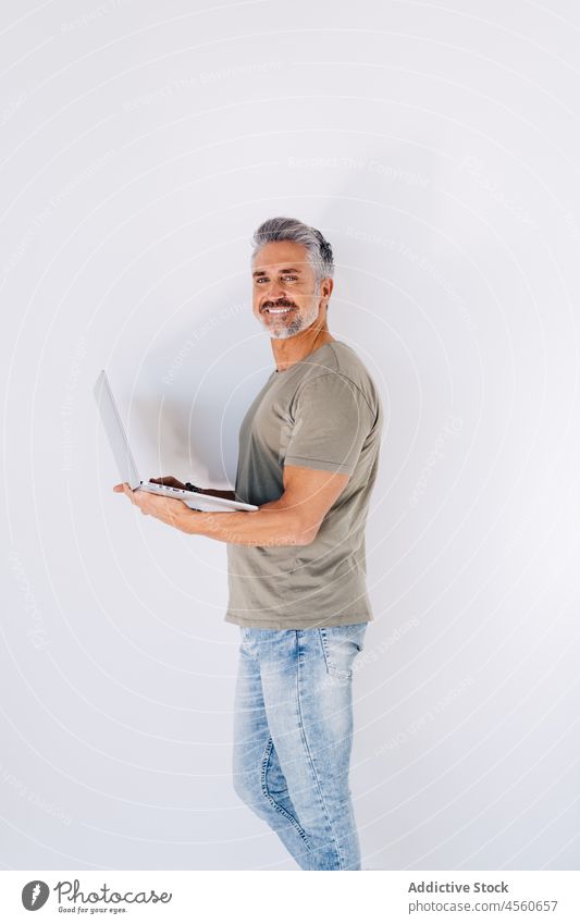 Focused old man with laptop near wall surfing browsing using elderly smile senior delight focus glad happy interest loft mature concentrate beard gadget jeans