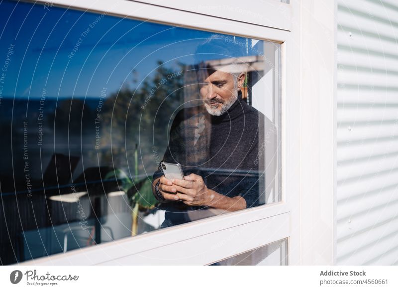 Aged male using mobile phone behind glass window man contemplate smartphone cellphone browsing witness curious attentive surfing elderly senior text message