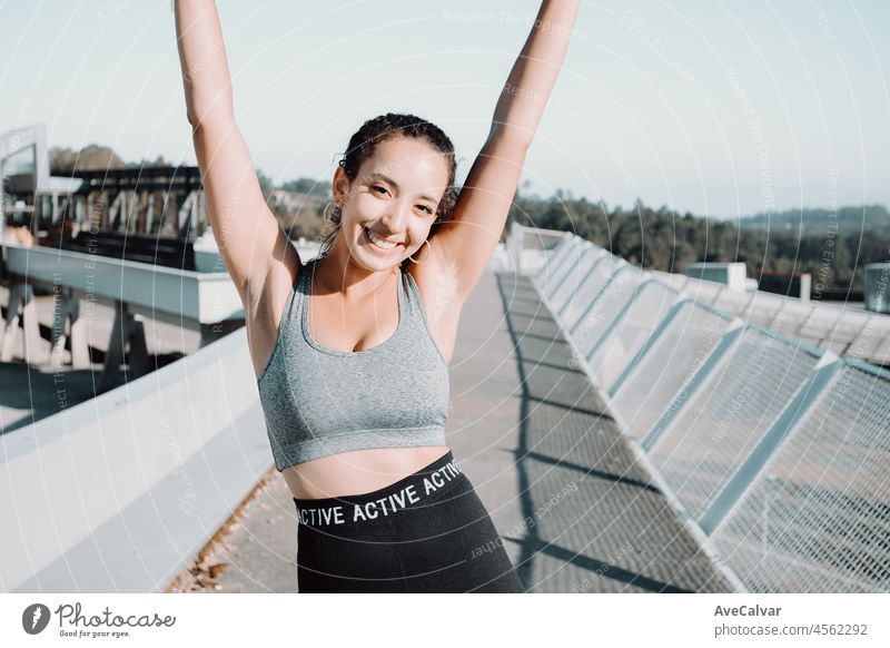 Beautiful girl athlete, african tanned skin. Happy celebrating after urban training. Waving arms, and smiling to camera. Safe exercise fresh air. Leggings clothing and top. Copy space image. beauty