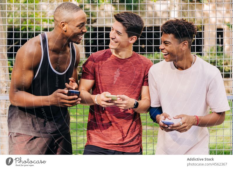 Diverse friends sportsmen browsing smartphones together and laughing in sportsground group people sportspeople athlete cheerful fit gadget sportswear stadium