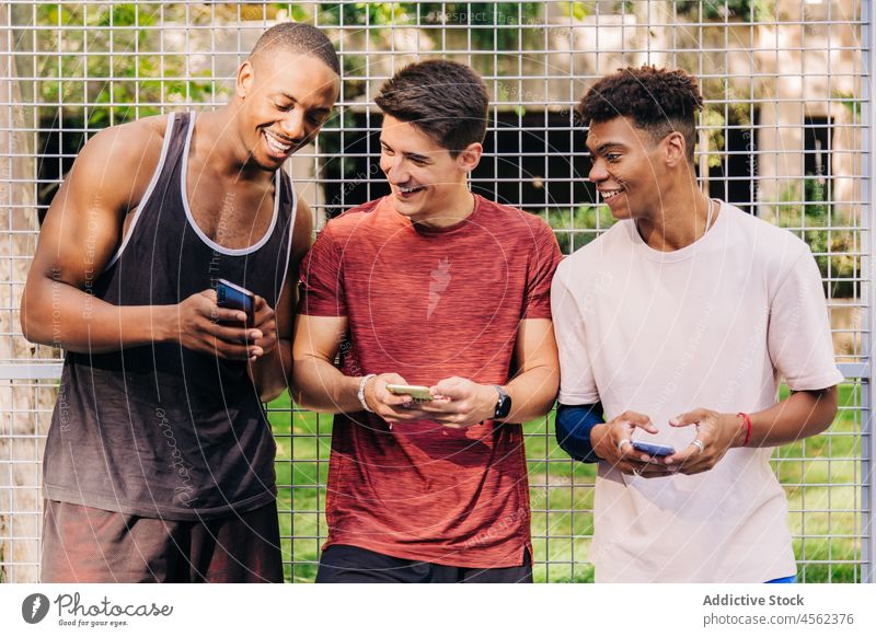 Diverse friends sportsmen browsing smartphones together and laughing in sportsground group people sportspeople athlete cheerful fit gadget sportswear stadium