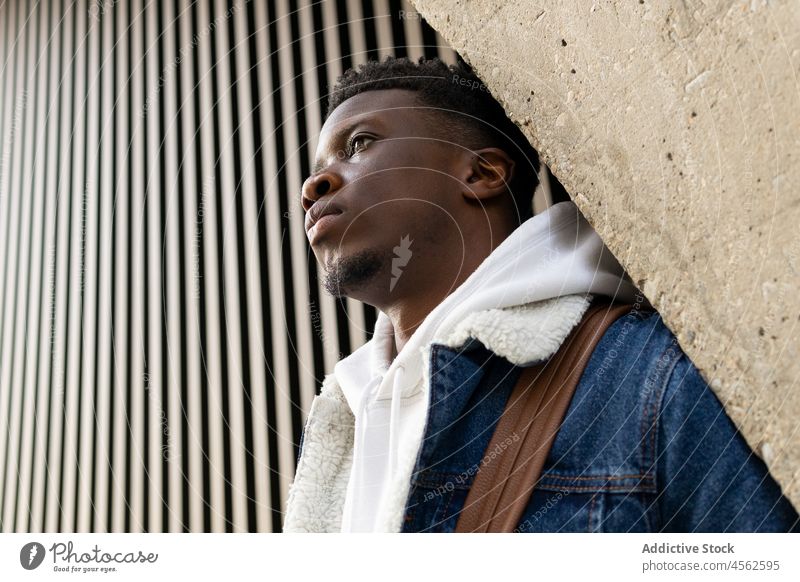 Stylish black male standing on street and leaning on wall man style trendy denim pensive building serious outfit thoughtful appearance african american