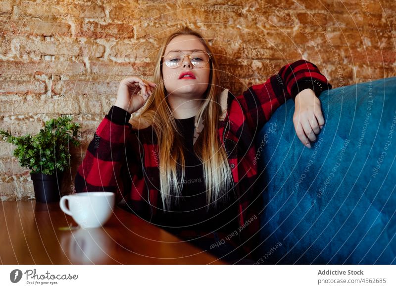Young woman sitting on a couch at cafe portrait young looking at camera restaurant blonde calm casual caucasian clothes coffee coffee shop colorful confident