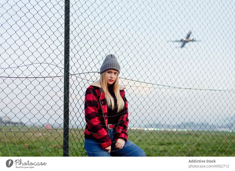Young woman leaning on the fence near to the airport young portrait looking at camera posing autumn cute female horizontal leisure lifestyle model outdoors