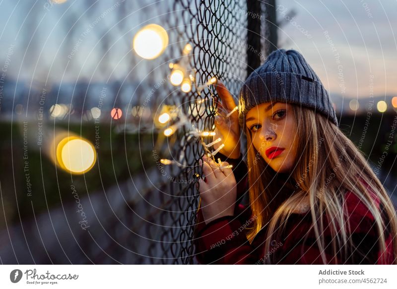 Young woman leaning on the fence and holding a light garland young portrait attractive autumn blonde bokeh bulbs caucasian city cute evening female horizontal