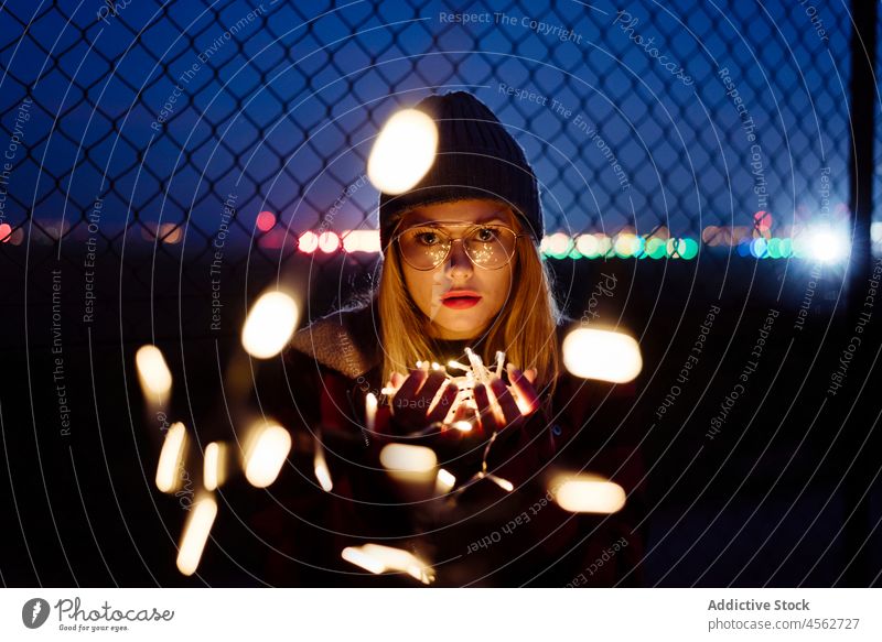 Young woman with wool hat and glasses holding a light garland young night portrait attractive autumn blonde bokeh bulbs candid caucasian city creativity cute