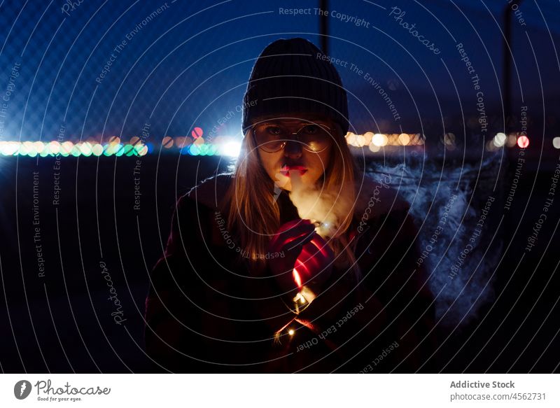 Young woman with wool hat and glasses holding a light garland young night portrait attractive autumn blonde bokeh bulbs candid caucasian city cold creativity
