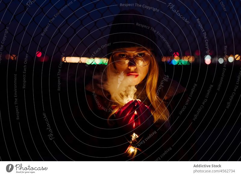 Young woman with wool hat and glasses holding a light garland young portrait night attractive autumn blonde bokeh bulbs candid caucasian city cold creativity
