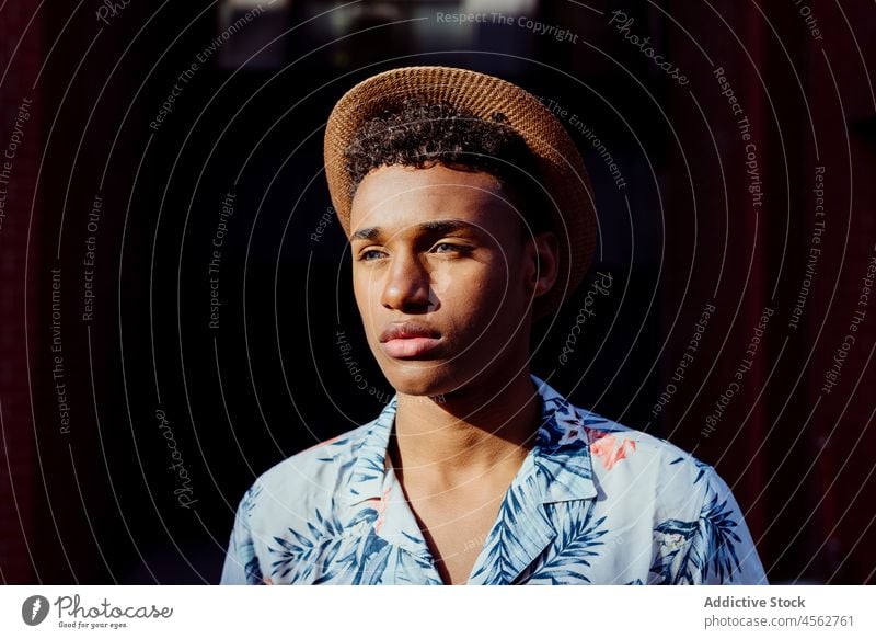 Trendy young black man portrait posing in the street male boy attractive handsome curly hair urban city hat summer summertime shirt floral sunny daylight
