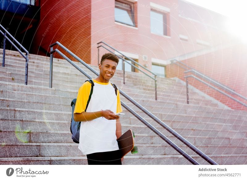 Young black student using smartphone on the street young male man boy happy walking ethnic smile skateboard african technology school sending american backpack