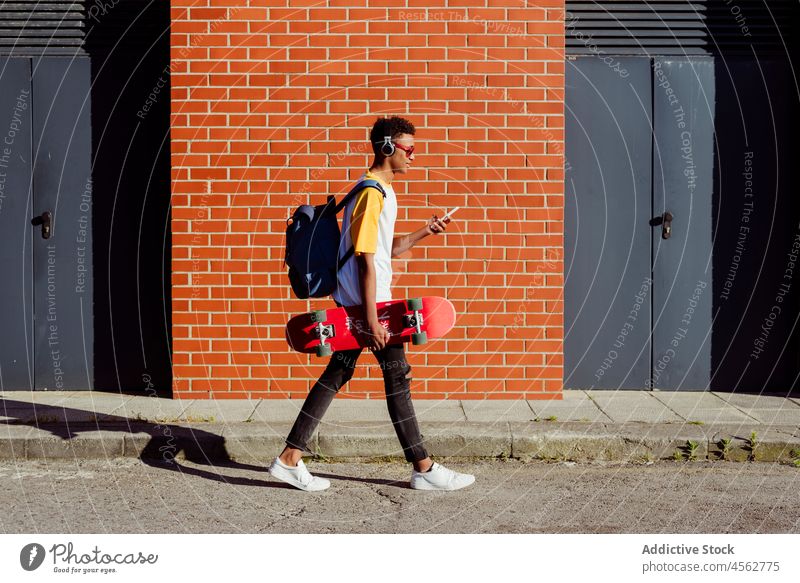 Young black man walking with headphones listening music on the street young male boy using smartphone browsing device mobile phone technology gadget school