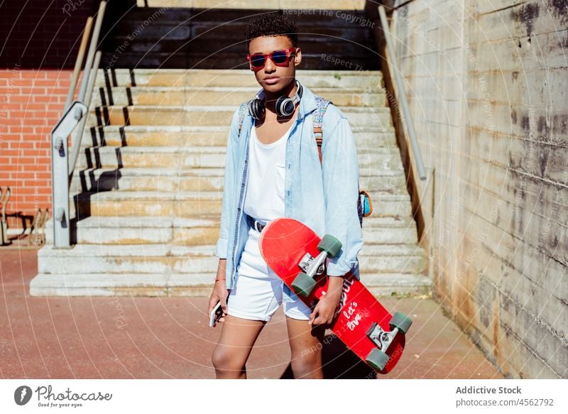 Young black man on the street holding a skateboard teenager student school american technology young happy shorts casual city leisure fashionable lifestyle male