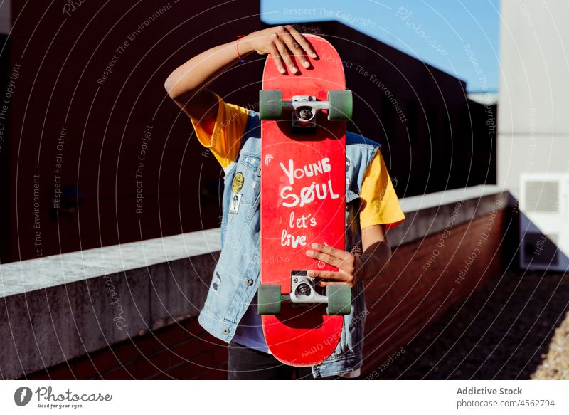 Young man hiding his face with a skateboard skateboarder rooftop unrecognizable city posing leisure lifestyle holding male boy patches faceless attractive fun