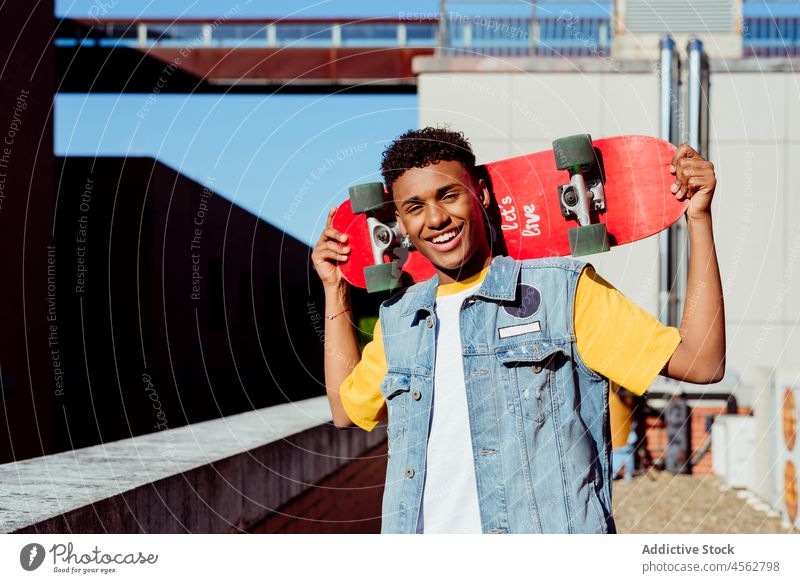 Handsome young black man with a skateboard on the street male boy happy smile portrait urban city brick wall rooftop vest handsome attractive colorful lifestyle