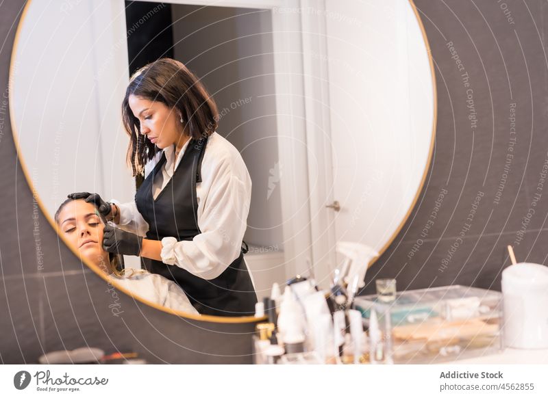 Female beautician brushing eyebrows of client in beauty studio women salon mirror care treat reflection professional pamper facial work procedure cosmetician