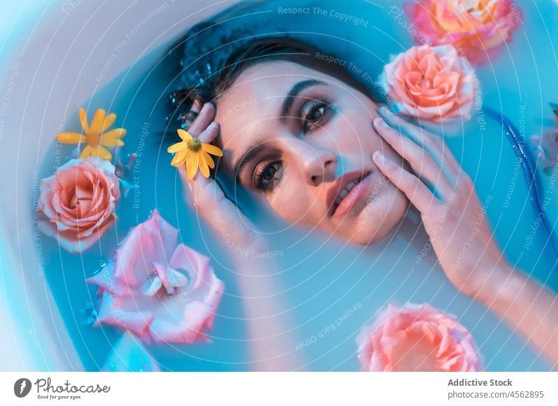 Young woman in bathtub with flowers in blue light wet hair sensual lying melancholy model seductive tender allure delicate tranquil relax gentle serene portrait