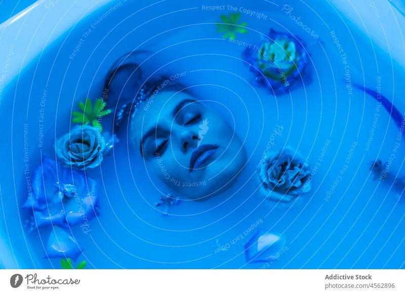 Young woman in bathtub with flowers in blue light wet hair sensual lying melancholy model seductive tender allure portrait delicate tranquil relax gentle serene