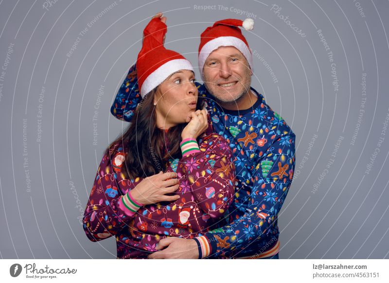Playful romantic middle-aged couple in colorful Xmas themed clothing celebrating Christmas and the Holiday Season in festive red Santa hats while enjoying a glass of sparkling champagne