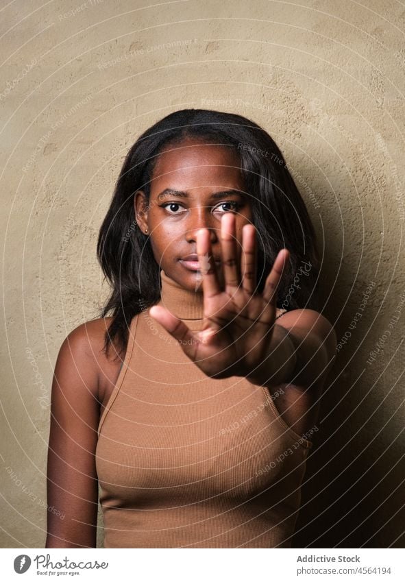 Serious black woman standing with raised arm against beige wall serious stop gesture sign arm raised concentrate restrict attention signal female