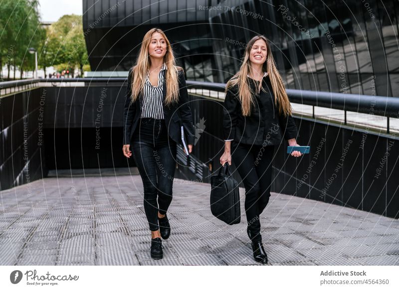 Cheerful businesswomen walking on street building pathway walkway spend time city urban modern coworker colleague positive female cheerful together content town