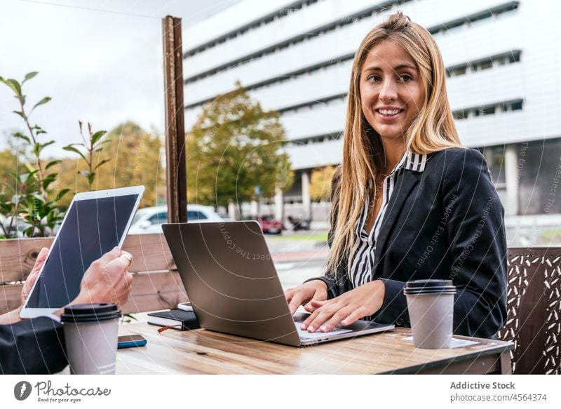 Positive woman browsing laptop near faceless colleague businesswoman cafe terrace tablet online coworker modern street spend time city spare time device gadget