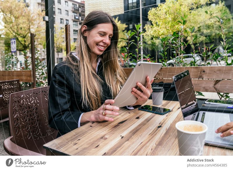 Cheerful businesswoman near faceless coworker at table with gadgets businesswomen cafe terrace tablet laptop online browsing modern street spend time city
