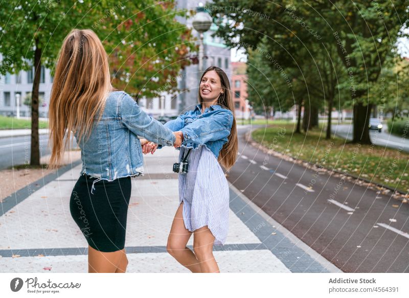 Content women spinning around on street friend photo camera spin around carefree having fun road spend time hobby city positive female cheerful together