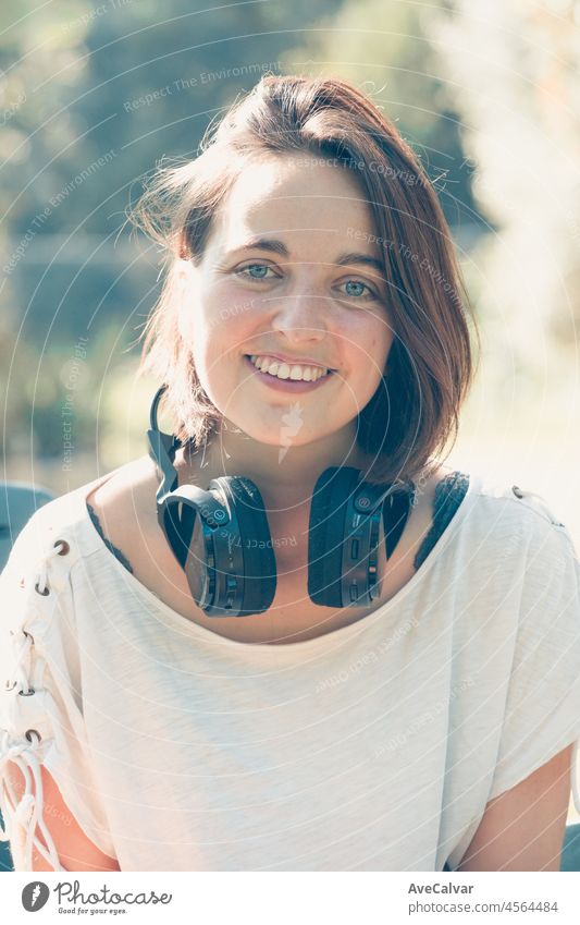 Girl listening to the music with headphones in a park smiling with pleasure as she listens to music in the garden enjoys favorite songs and beautiful nature. During sunset music concept. Close portrait