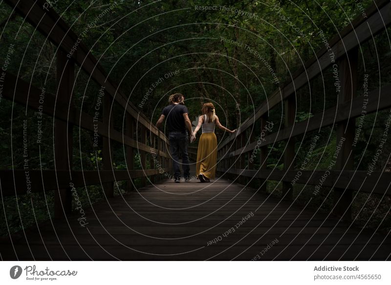 Young loving couple embracing and kissing on wooden footbridge spain galicia mao forest holding hands relationship romantic nature river walkway boyfriend