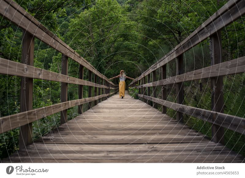 Young woman standing on wooden footbridge in green mountainous valley river mao galicia sacra spain traveler nature tourism tourist explore trip adventure