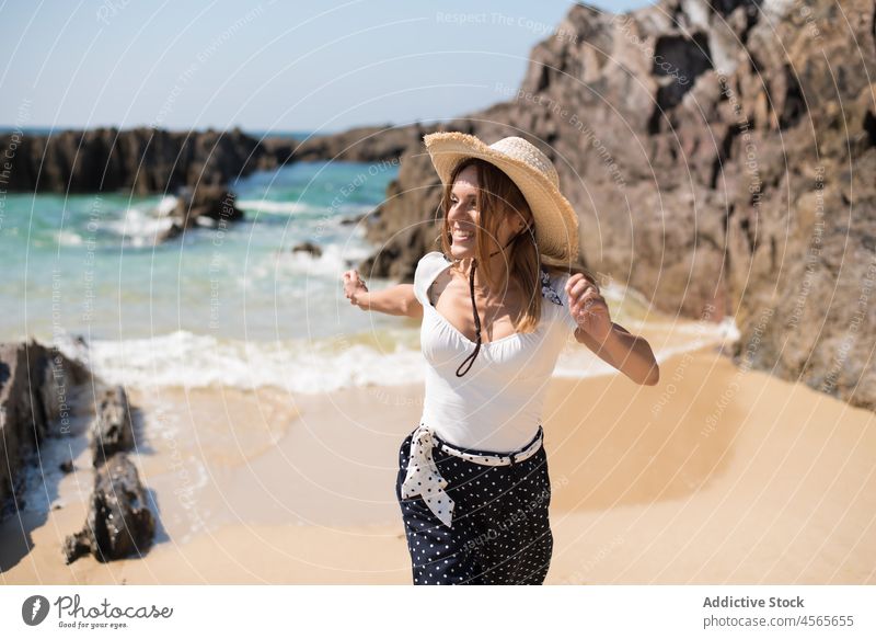 Cheerful woman walking on sandy beach with cliffs in summer straw hat spain galicia praia furnas vacation holiday tourist seashore travel daytime rest joy coast