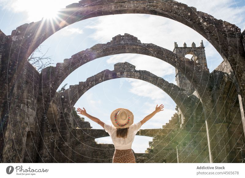 Positive woman in hat raising hand in arched passage spain construction santa marina dozo gothic church galicia stone historic traveler heritage structure