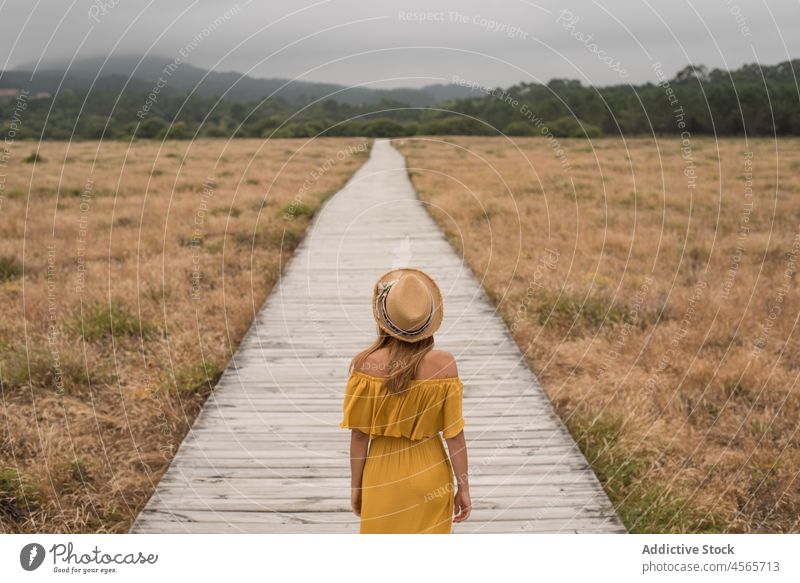 Anonymous woman walking on boardwalk in countryside dune footpath nature meadow grass corrubedo galicia female spain wooden field summer dress rural vacation
