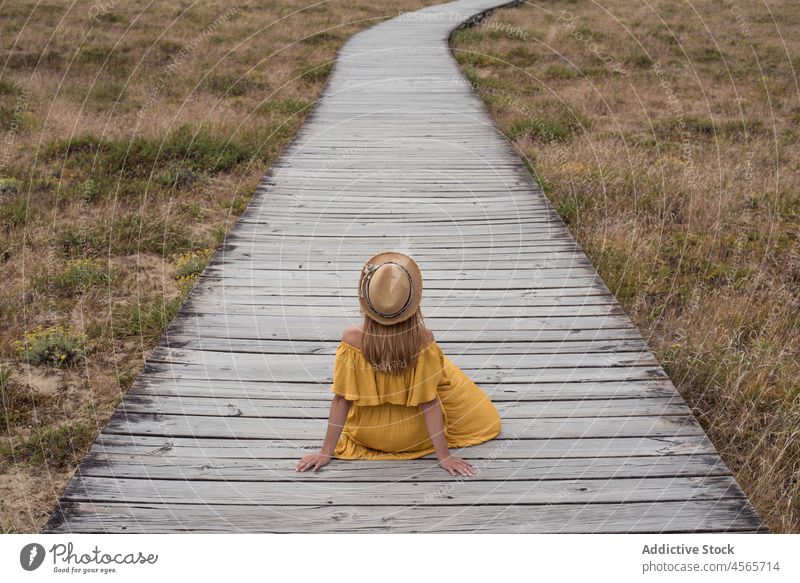 Anonymous woman sitting on boardwalk in countryside dune footpath nature meadow grass corrubedo galicia female spain wooden field summer dress rural vacation