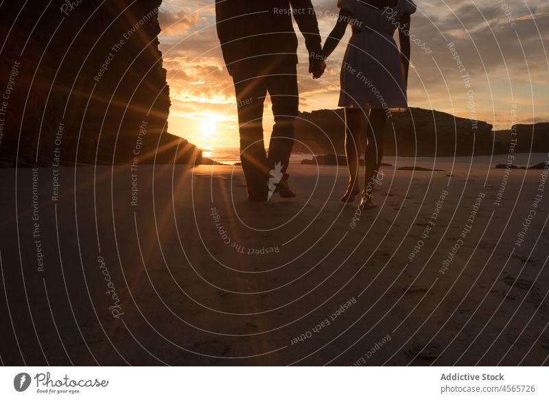 Anonymous couple walking on beach in evening silhouette sundown sunset together twilight shore picturesque holding hands beach of the cathedrals galicia spain