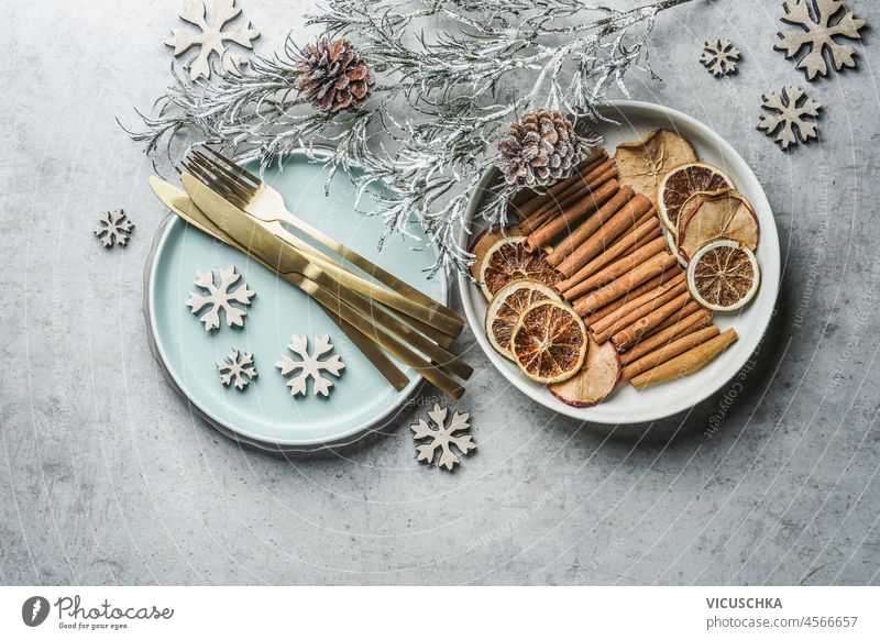Christmas table setting with golden cutlery, pale blue plate, cinnamon sticks, dried orange natural dried apples and oranges and winter branches on grey table.  Top view.