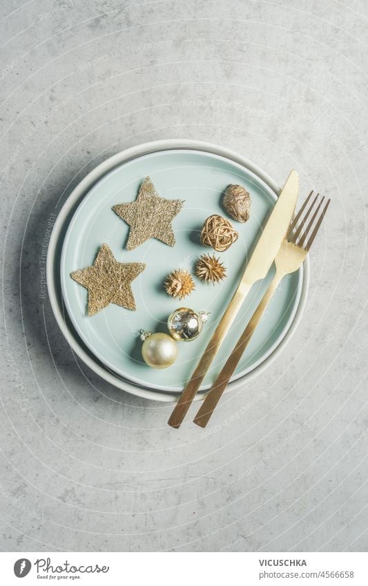 Christmas table setting with golden cutlery, pale blue plates, decoration with stars and baubles on grey concrete table. Festive dinner. Top view. christmas