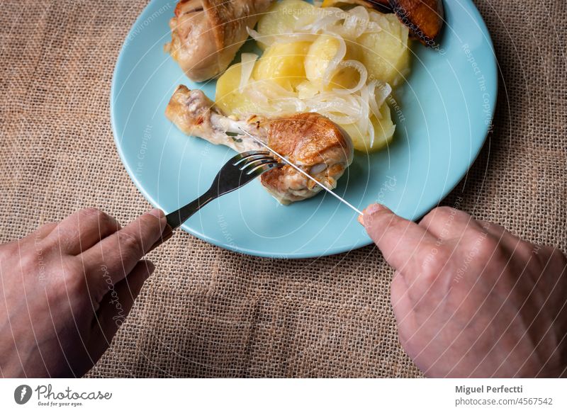 Woman's hands cutting a lemon chicken thigh on the plate, garnished with potatoes and onion woman cooked eat oven dish fat-free healthy food meal dinner