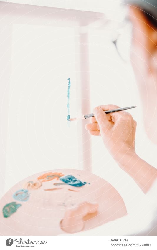 Close-up of Female senior old Artist Hand, Holding Paint Brush and Drawing Painting with blue Paint. Colorful, Emotional Oil Painting. Contemporary Painter Creating Modern Abstract Piece of Fine Art