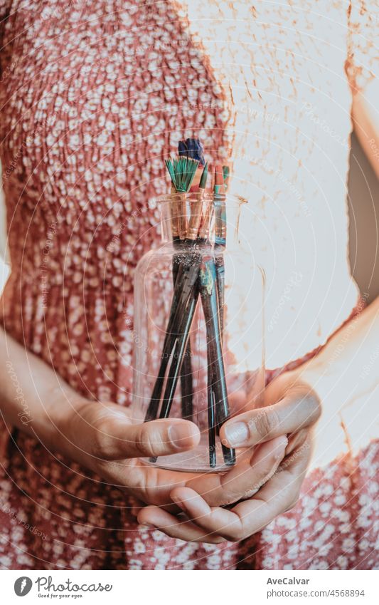 Young woman artist hands grabbing a bottle filled with paint pencils and brushes, ready for painting acrylic. Artistic concepts, artist concept. Beauty dress concept vintage with sun bean