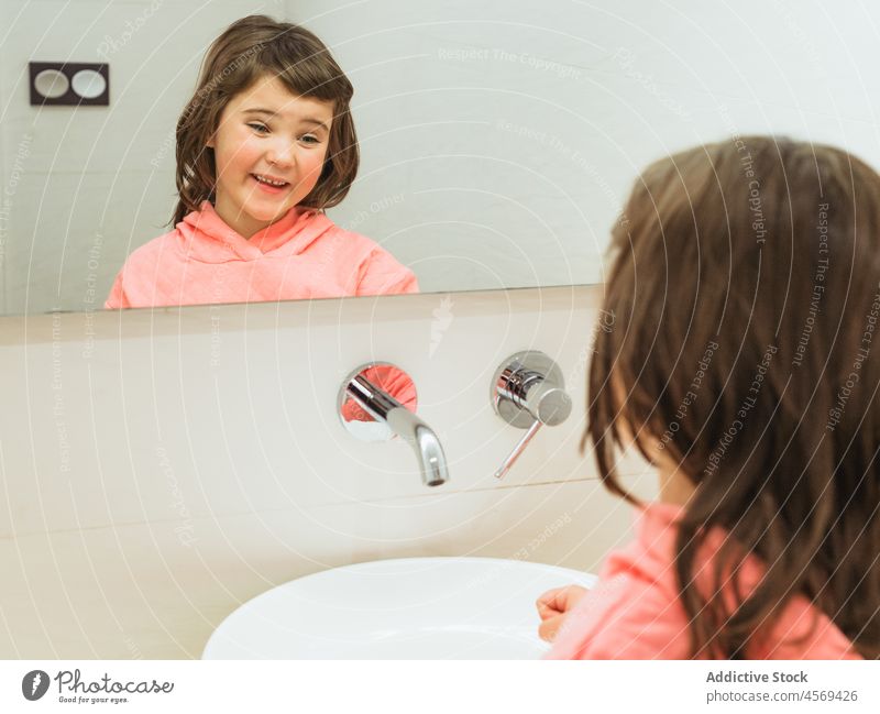 Cheerful girl looking at mirror in bathroom kid hygiene everyday routine daily domestic reflection positive smile optimist sink washbasin care home clean