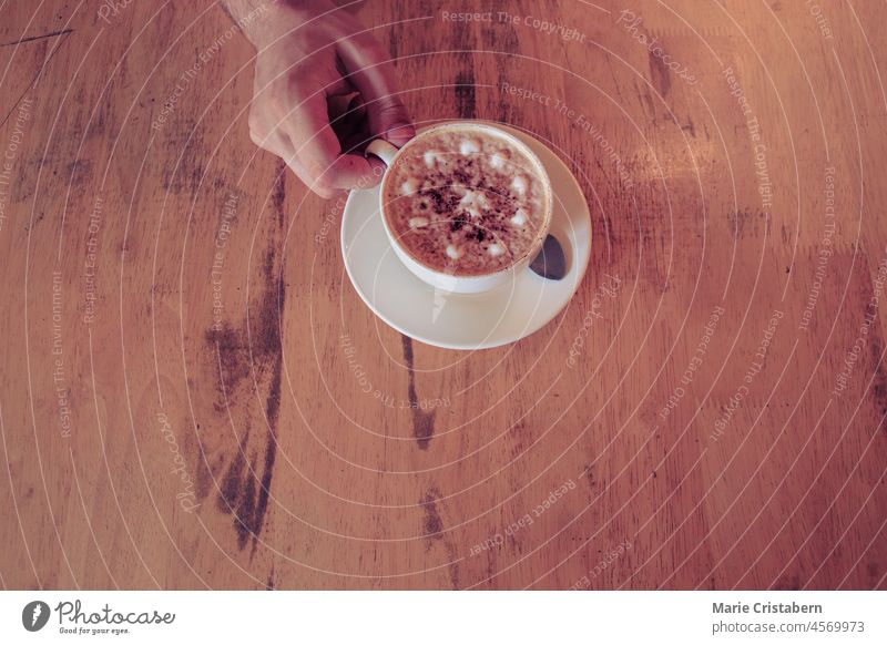 Top view of hand holding a freshly made cup of frothy cappuccino in a cafe cafe culture top view copy space coffee background beverage frothy coffee flavor