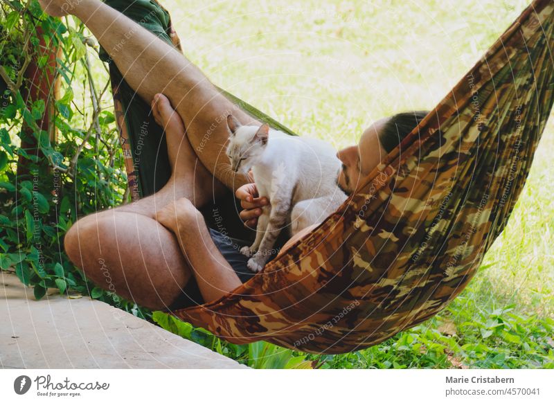 A man relaxing in the hammock with his pet siamese cat 30-34 year old leisure pet owner togetherness comfortable lifestyle unwinding wellness peaceful chill out