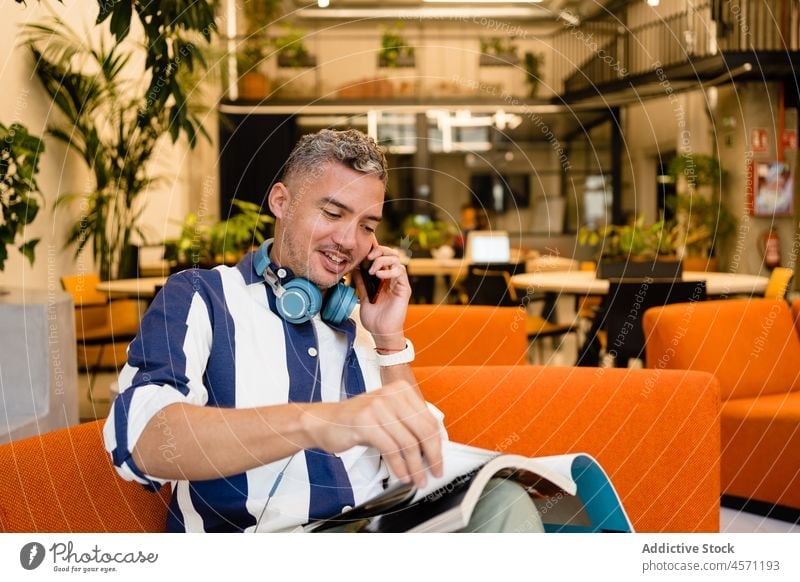 Man reading magazine while having phone call in office man smartphone conversation communicate work worker using gadget device employee workplace male workspace