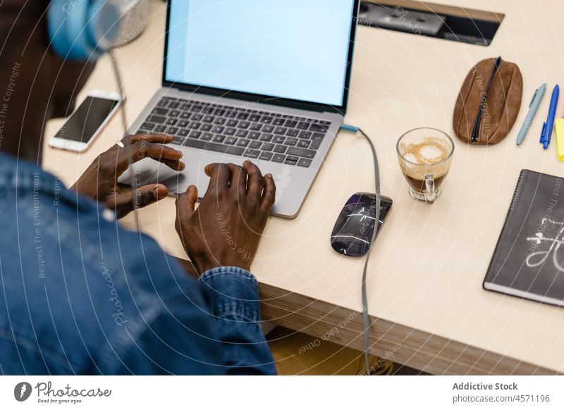 Anonymous black man in headphones working on laptop music office typing internet online browsing worker using gadget device listen netbook coffee employee