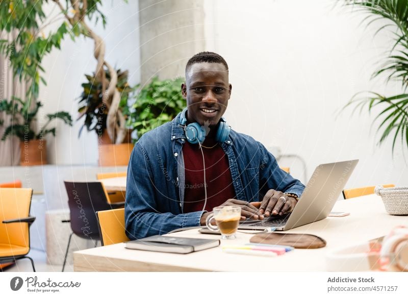 Black man with headphones working on laptop office typing internet online browsing worker using gadget device netbook coffee employee attentive surfing