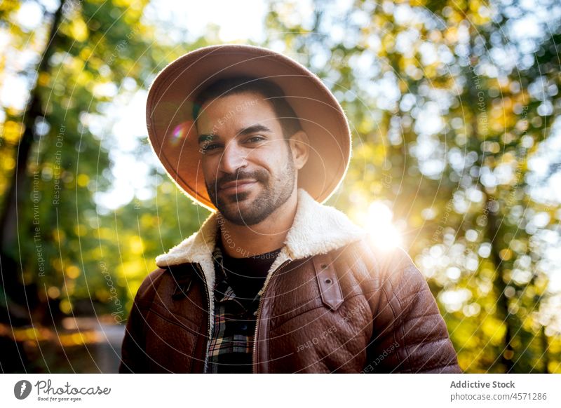 Happy hipster guy standing in woods with green trees man nature style grove adventure trip recreation leisure outfit trendy hat summer wear male apparel