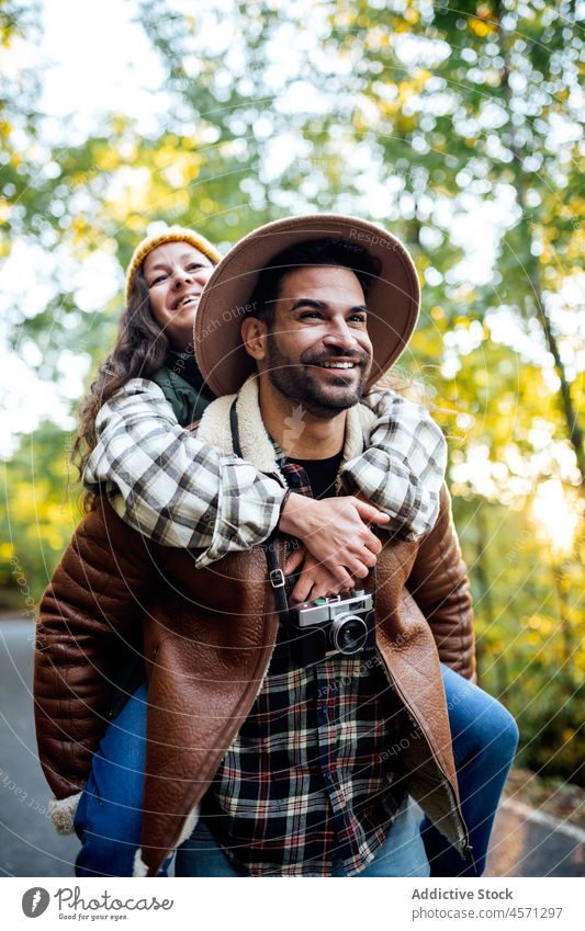Man giving piggyback ride to girlfriend in nature couple having fun road tree trip adventure relationship traveler cheerful together boyfriend content grove
