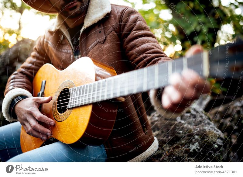 Hipster guy playing guitar in green woods in nature man music instrument forest song tree hobby guitarist musician male melody hat leisure talent skill