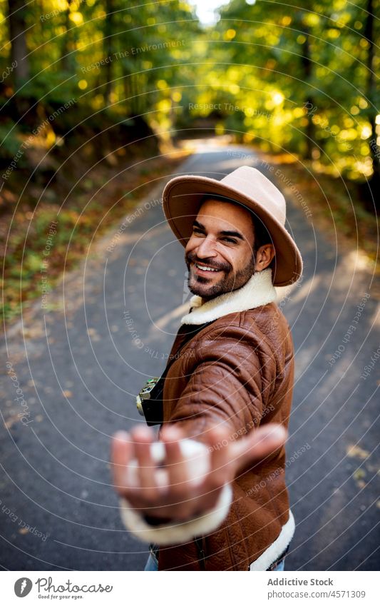 Smiling man on road in nature reach out tree follow me path style grove adventure trip recreation leisure outfit trendy hat summer cheerful asphalt wear content